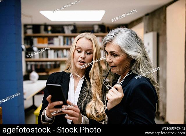 Mature and young businesswoman using smartphone in loft office