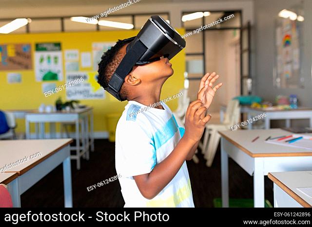 Side view of african american elementary schoolboy gesturing while wearing vr glasses in classroom
