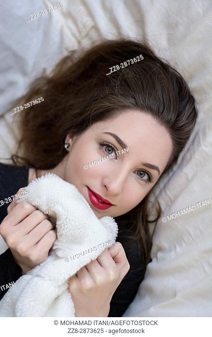 Beautiful young woman laying down in bed holding the blancket