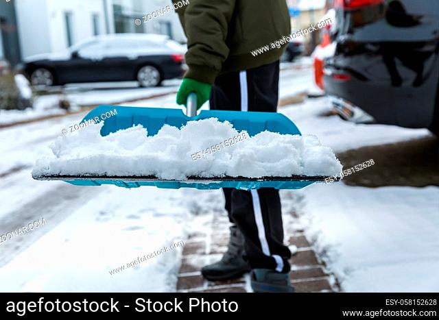 Child shoveling and removing snow in front of his house in the suburb