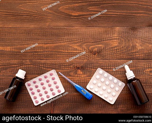 medications or tablets and drops and electronic thermometer on a dark wooden background with copy space. Flat lay or top view