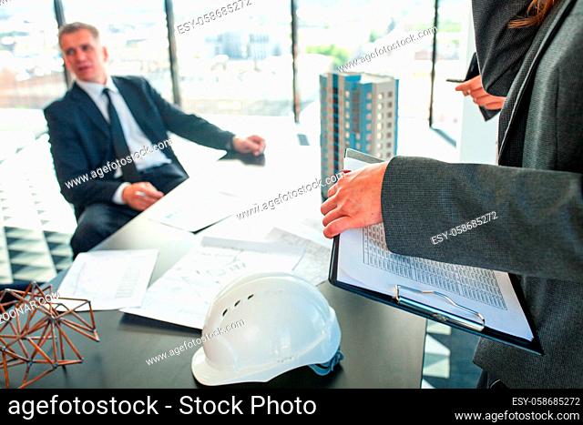Meeting of architects and business investors, model of modern multi storey residential building house plans and hardhat on table , construction planning concept