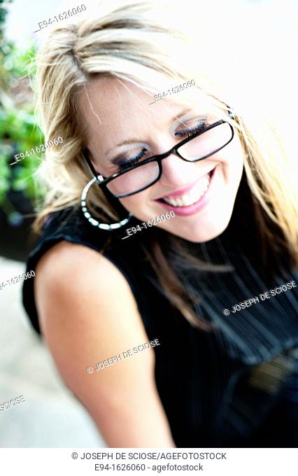 Close in shot of a 31 year old blond woman wearing reading glasses with a flirty smile, eyes looking down