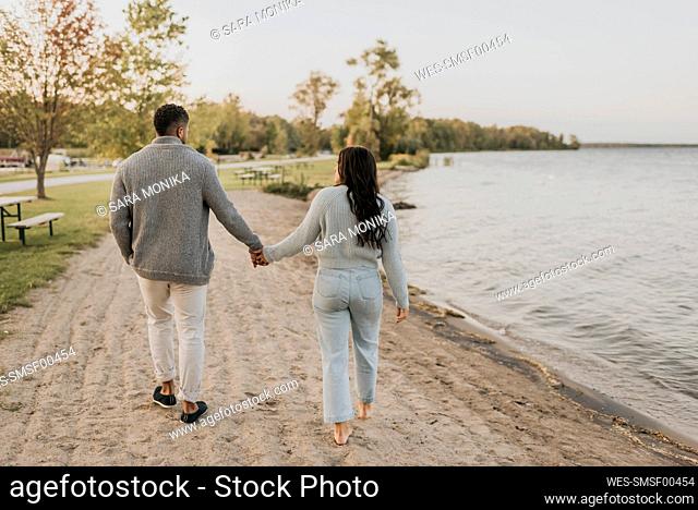 Couple holding hands while walking by lake