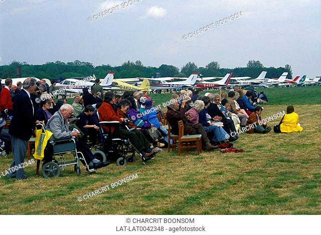 Air show. Row of light planes. Crowd. Seated and standing. Two wheelchairs