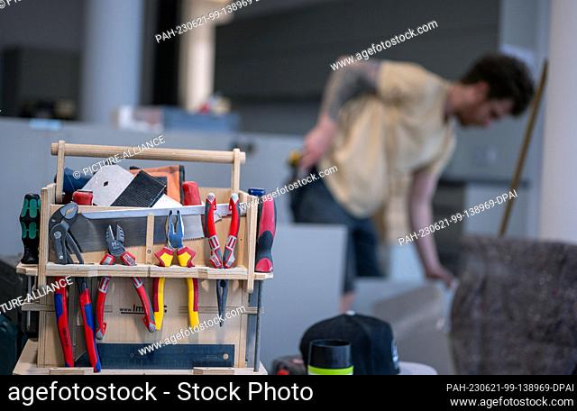 19 June 2023, Berlin: A toolbox sits on the table while a craftsman assembles a piece of furniture in the background. Photo: Monika Skolimowska/dpa