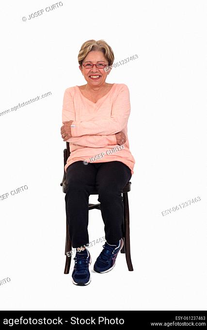front view of a full portrait of happy senior woman sitting on chair dressed in sportswear on white background