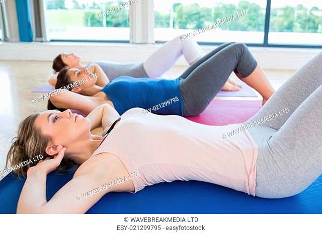 Women doing sit ups on exercise mats in fitness studio