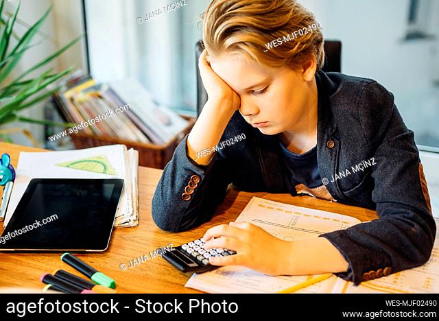 Frustrated boy sitting at desk with workbook and pocket calculator