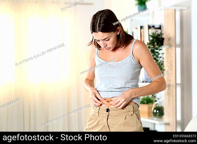Woman worried about body fat touching her belly standing at home