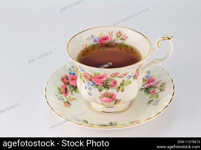 Full antique teacup and saucer with rose and gold decoration isolated on white