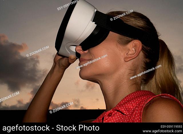 Closeup portrait of woman having fun with virtual reality glasses over beautiful summer sunset sky tree