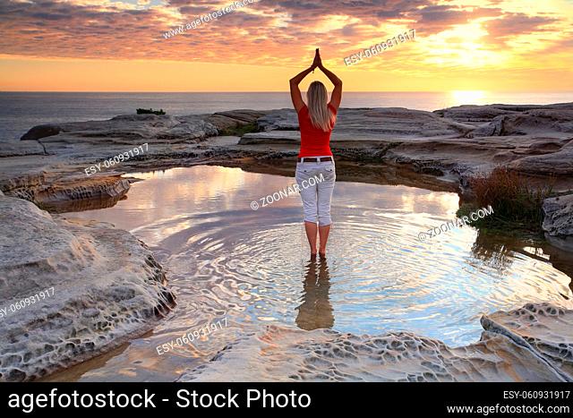 A woman standing by the ocean at sunrise, practicing yoga, meditation, pose. Rejuvenating the soul, quiet time and solitude in natures beautiful surrounds