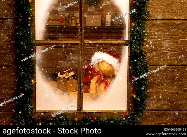 Looking through the frosty window of Santa Claus North Pole workshop with toys on work bench in front of brick fireplace. Horizontal with snow effect