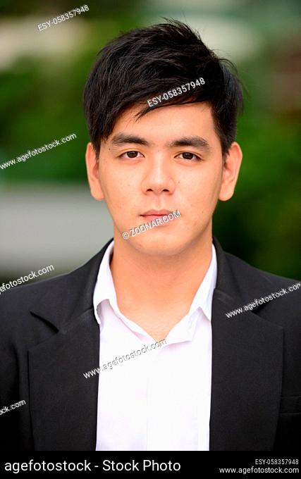Portrait of young handsome Filipino businessman at the park in the city outdoors