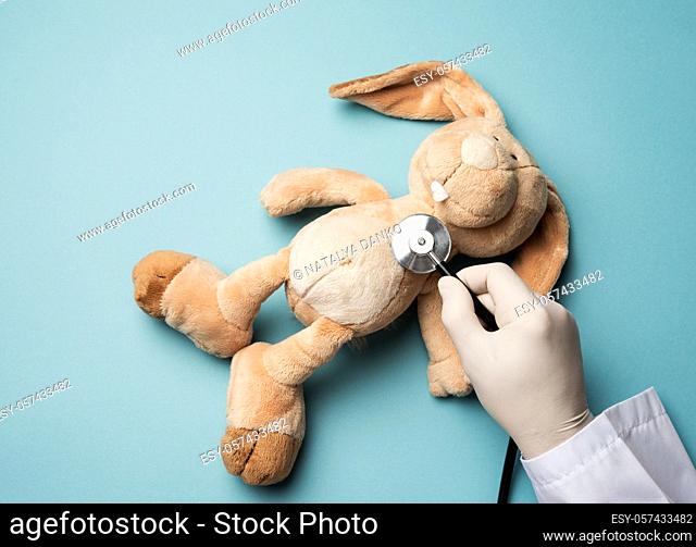 plush rabbit lies on a blue background, a male hand in a white latex glove holds a medical stethoscope, top view, pediatrics