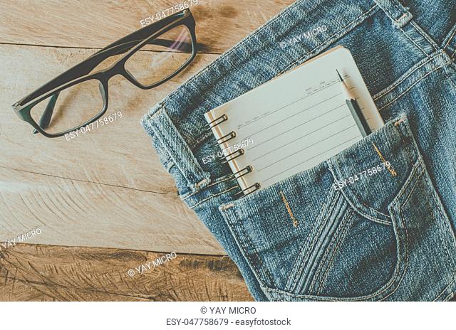 Notebooks and pencils in pocket jeans and glasses on a wooden floor