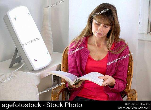 Woman sitting reading near a light therapy lamp