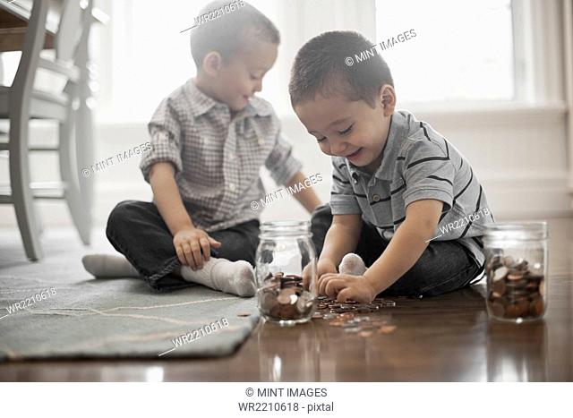 Two children playing with coins, dropping them into glass jars