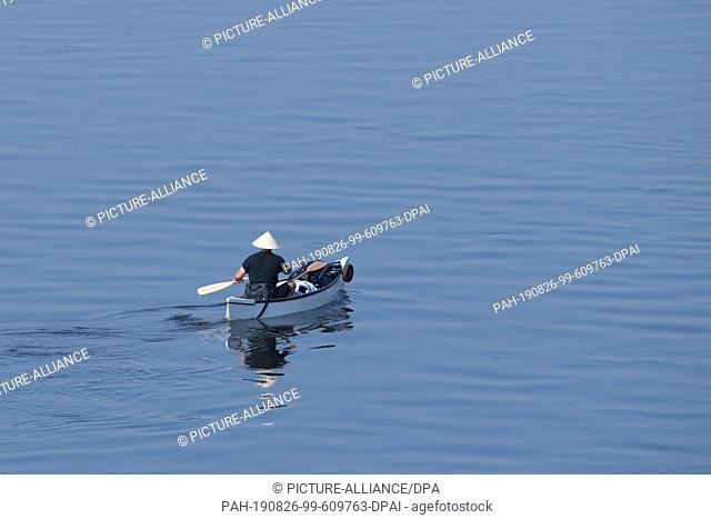 26 August 2019, Saxony, Dresden: A man with an Asian cone hat drives in a paddle boat on the Elbe. Photo: Sebastian Kahnert/dpa-Zentralbild/dpa