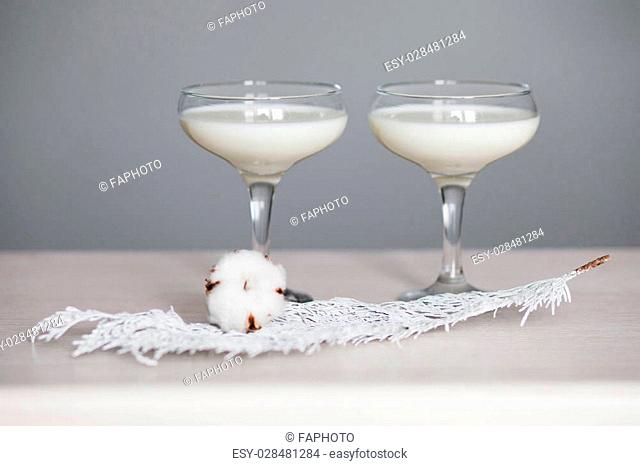Two glasses filled with milk and put together with a cotton flower and thuja