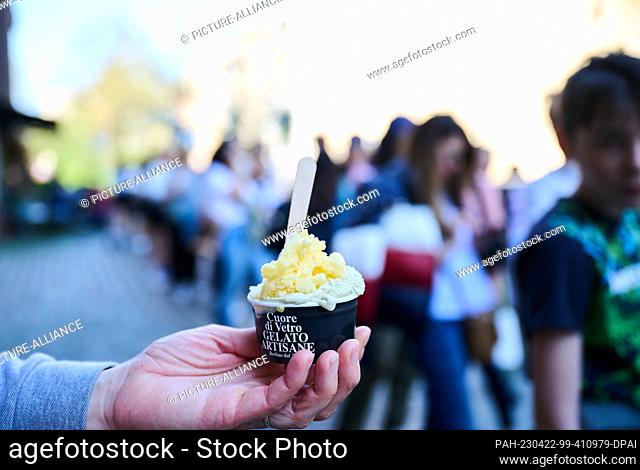 22 April 2023, Berlin: A mother holds her ice cream with the varieties orange and pistachio while the crowd behind her exceeds fifty