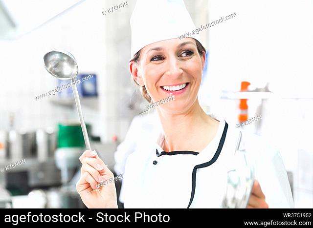 Smiling chef in commercial kitchen waving ladle