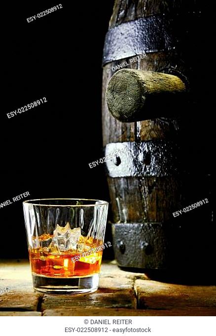 A glass of whiskey with ice and an oak barrel