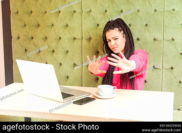 Stop doing it. Portrait of aggressive scared young girl freelancer with black dreadlocks hairstyle in pink blouse sitting with bad mood, pleased you make pause