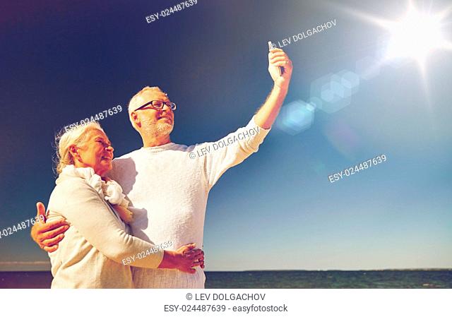 age, travel, tourism, technology and people concept - happy senior couple with smartphone taking selfie on summer beach