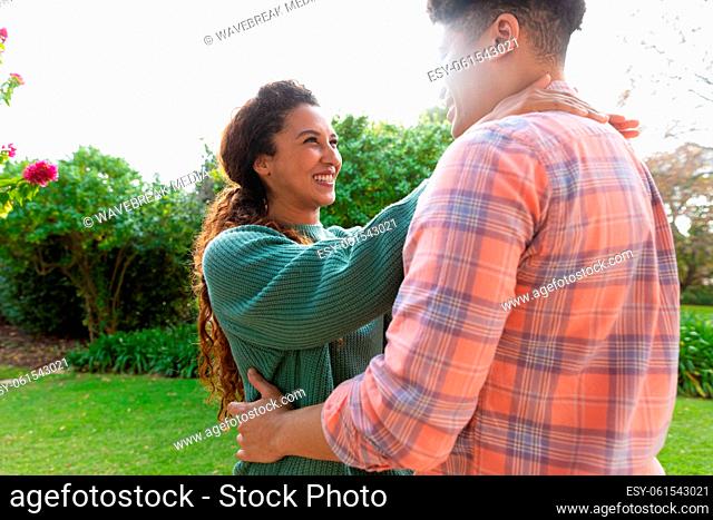 Happy biracial couple embracing and smiling on terrace in garden