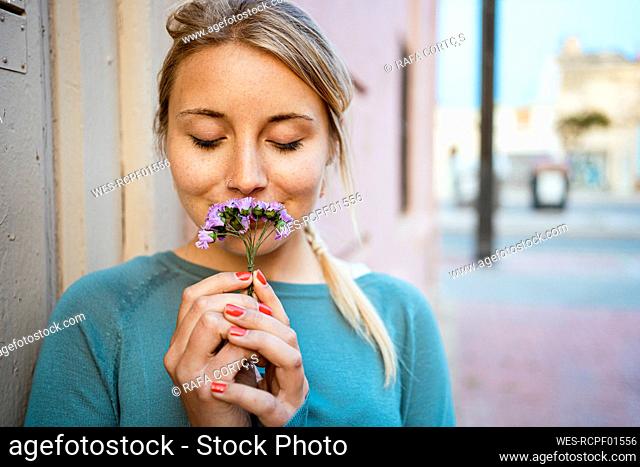 Beautiful woman with eyes closed smelling small flowers at footpath