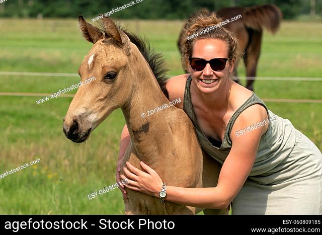 Young woman cuddling with her best friend, falcon color stallion foal, sharing love and mutual affection