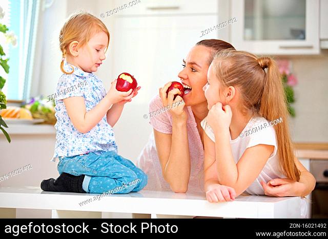 Glückliche Mutter und ihre Kinder essen Apfel zusammen in der Küche