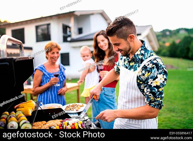 Portrait of multigeneration family outdoors on garden barbecue, grilling and talking