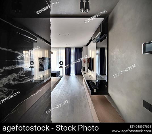 Modern room with concrete, marble and white walls. There are wooden lockers, a black niche with books, white rack with flower and decorations, TV, fireplace