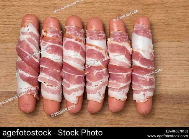 Preparation of raw sausages wrapped spirally in bacon on a wooden background. Top view