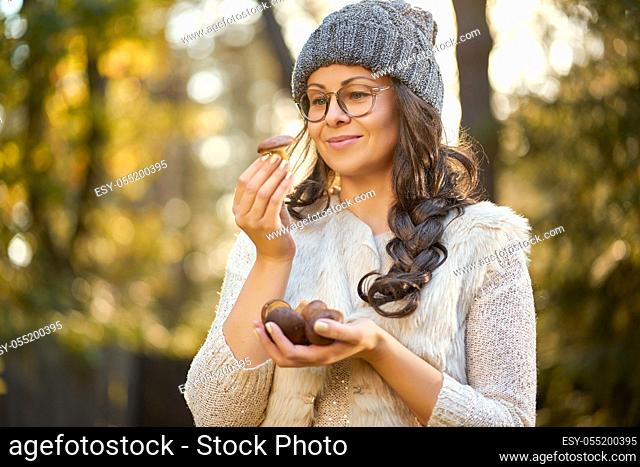 beautiful woman in cap and glasses is holding mushrooms in hands in autumn forest