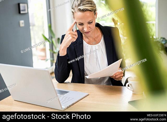 Businesswoman with laptop checking document while working at office