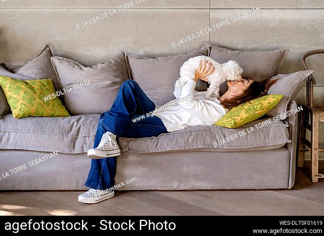 Woman playing with her dog while lying on sofa