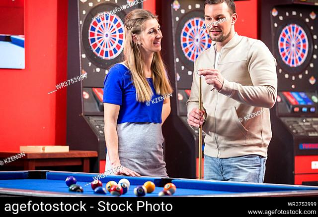 Happy wife looking at husband while playing billiard in club