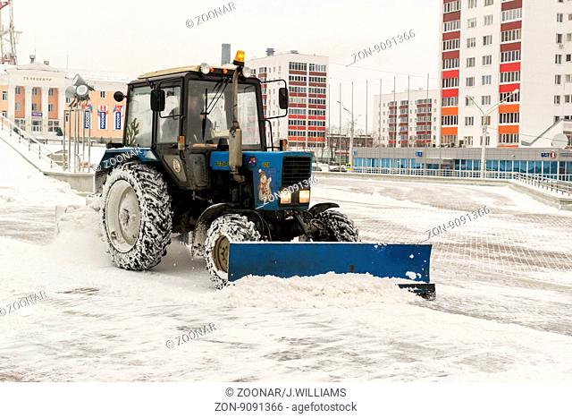 UFA - RUSSIA 27TH DECEMBER 2015 - Blue tractor uses a front shovel and hydraulic driven brush to clean snow from a concrete car park in Ufa