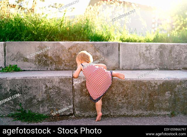 Little girl in a dress climbs high stone steps in the park. High quality photo