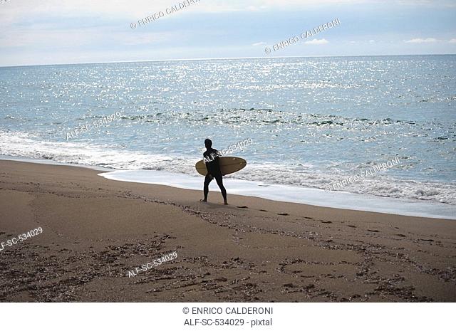 Young man walking along shoreline with his surfboard