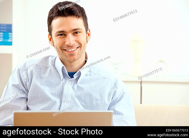 Happy young man working on laptop computer, smiling