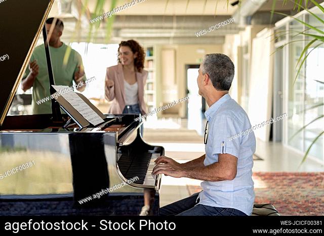 Mature businessman playing piano looking at colleagues enjoying in office