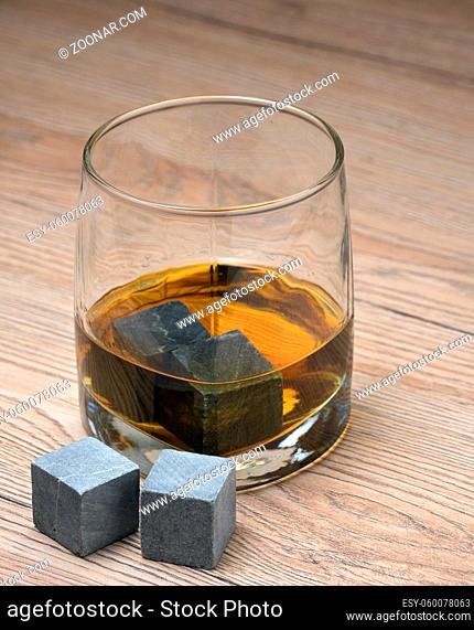 Glass with whiskey and whiskey stones on wooden background