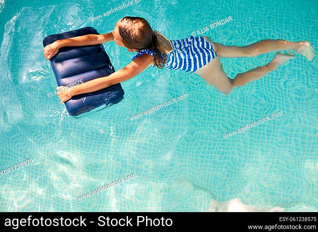 Happy little girl having fun in the swimming pool, dives and swim, summer vacation at home, tropical holiday resort
