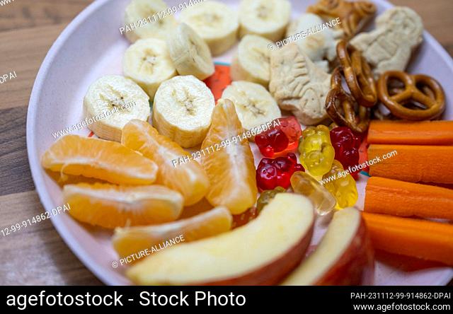 ILLUSTRATION - 08 November 2023, Saxony, Leipzig: ILLUSTRATION - A plate of snacks, fruit, vegetables and sweet nibbles sits on a kitchen table