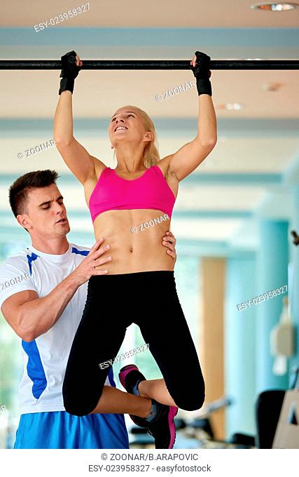 trainer support young woman while lifting on bar in fitness gym